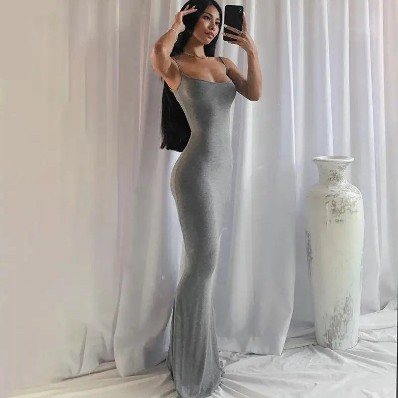 Woman in a silver evening gown taking a mirror selfie against a white curtain.